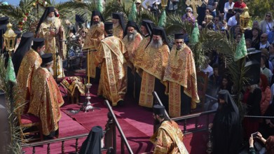 Priests in golden robes stand on a stage during a religious ceremony, surrounded by a large crowd,