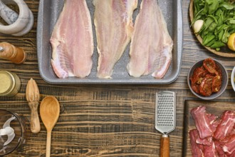 Fresh fish fillets are laid out on a baking tray, surrounded by various ingredients including