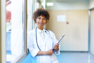 Female doctor standing confidently in a bright hospital corridor, holding a medical chart and