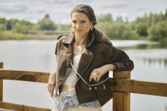 A model stands confidently near a tranquil water body, showcasing a fashionable outfit complete