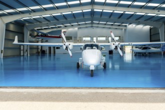 White twin engine airplane parked inside a spacious hangar, featuring a bright blue floor and
