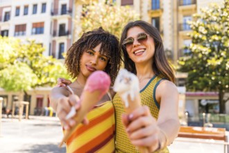 Two friends enjoying a sunny day in the city, happily holding and sharing colorful ice cream cones