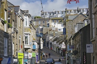 A busy town street with traditional stone houses and many passers-by, holiday resort, St Ives,