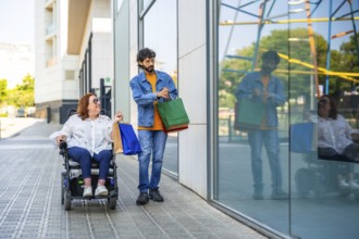 Couple walking on city sidewalk after shopping, woman using a wheelchair and carrying colorful bags