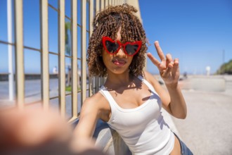Young woman with heart shaped sunglasses takes a selfie while making the peace sign, leaning