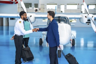 African pilot shaking hands with a businessman inside an aircraft hangar, both holding trolley
