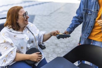 Happy customer using a credit card for contactless payment at an outdoor cafe, assisted by a