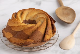 Fresh marble bundt cake, cake next to a rustic wooden spoon on a light-coloured background