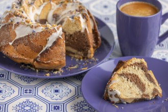 Cut marble bundt cake, cake on blue plates with icing, next to a blue cup of coffee