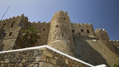 Medieval stone castle with palm trees and blue sky, imposing architecture, Monastery of St John the