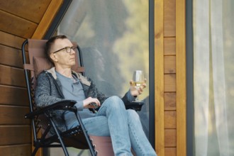 Middle-aged man relax on terrace of a tiny house with a glass of wine