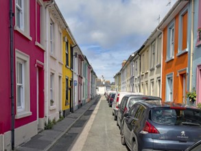 Bunte Reihenhäuser auf einer ruhigen Straße, geparkt mit Autos und blauem Himmel, Penzance,