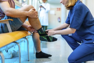 Female nurse bandaging a male patient's injured ankle in a hospital setting, providing support and