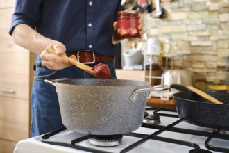 A person prepares a homemade meal adding tomato paste to a pot on the stovetop in a bright, modern
