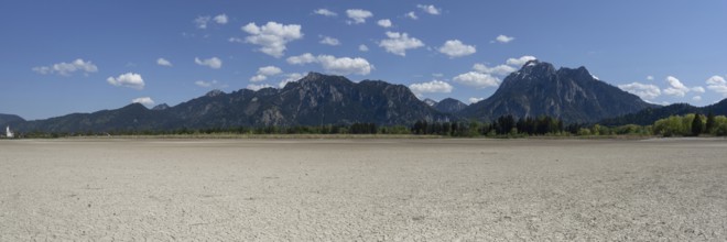 Cracked, dried out ground, waterless Forggensee in spring, behind it Tegelberg massif and Säuling,