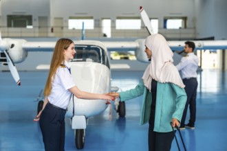 Female pilot shaking hands with a muslim businesswoman inside an aircraft hangar, symbolizing