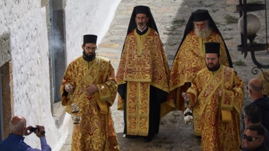 Four clerics in splendid gold robes walk down a narrow alley surrounded by spectators, Orthodox