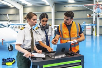 Aircraft maintenance engineer showing data on laptop to two female pilots in hangar, discussing
