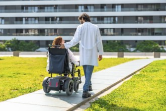 Doctor assisting a female patient in a wheelchair, strolling through a modern hospital's green