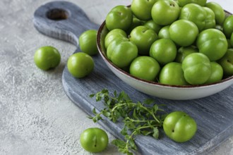 Tkemali, green cherry plum, in a bowl, on a gray table, top view, natural light, no people