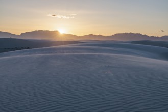 Rays of light over the mountains highlight windblown sand at sunset at White Sands National Park in