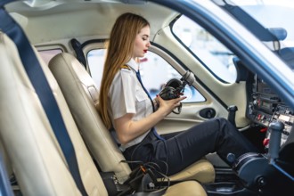 Young woman pilot checking her headset while sitting in the cockpit of a small aircraft, preparing
