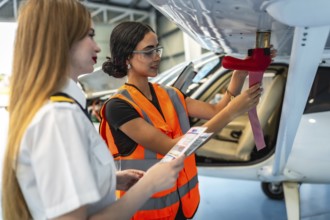 Female aircraft maintenance engineer inspecting airplane wing with pilot assisting, holding