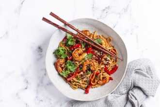 Udon noodles, shrimp with vegetables and fresh herbs, in a bowl with chopsticks, light background,