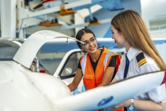 Female pilot and aircraft maintenance technician working together in hangar, discussing maintenance