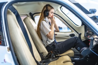Female pilot sitting in the cockpit of a small aircraft, wearing a headset and communicating,