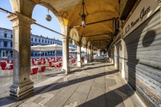 Chairs and tables of cafes, arcades at St Mark's Square in the morning light, Venice, Veneto,