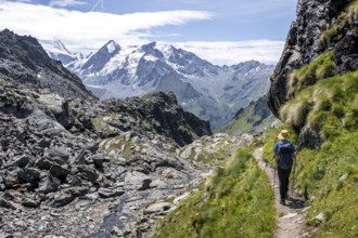 Mountaineer on hiking trail in mountain landscape, descent at Col du Louvie, view of the summit of