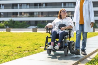 Doctor assisting a patient in a wheelchair, enjoying a sunny day in a city park, promoting