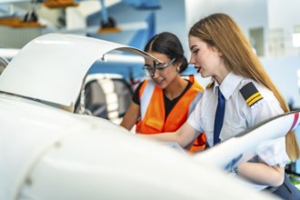 Female pilot and an aircraft maintenance engineer are inspecting the engine of a small plane in a