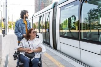 Caregiver pushing a smiling woman in a wheelchair at a modern tram station, both eagerly waiting to