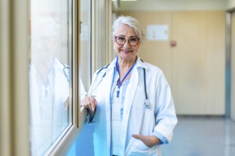 Portrait of a confident senior female doctor standing in a bright hospital corridor, representing