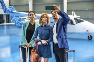 Three businesspeople are taking a selfie with a smartphone in a hangar with a private jet and