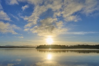 Sunlight breaks through the clouds in the morning over a calm lake, Lake Mahinapua, Ruatapu, South