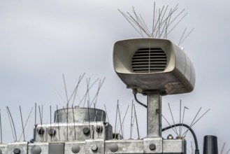 Loudspeakers on a scoreboard, at a railway station, studded with thin wires against birds, pigeons,