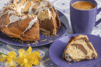 Cut marble bundt cake, cake on blue plates with icing, next to a blue cup of coffee
