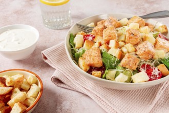 Caesar salad with salmon, with croutons and dressing, in a salad bowl, on a pink table