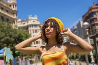 Young woman adjusting her yellow beanie in valencia city center, enjoying a sunny summer day