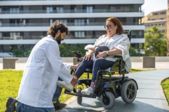 Male doctor is adjusting the footrest of an electric wheelchair for a smiling woman, promoting