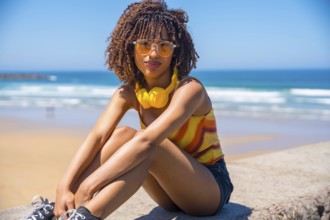 Fashionable young woman enjoying the summer sun and music on a beach wall, embracing the carefree
