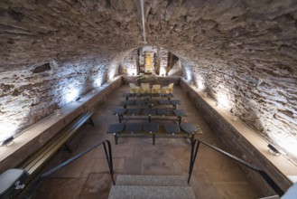 Rustic wine cellar with stone walls and vaulted ceiling, seating is provided for a presentation,