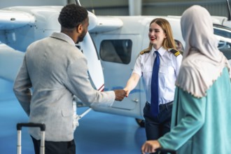 Female pilot shaking hands with businessman next to a private airplane inside an hangar, a