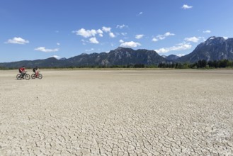 Cracked, dried out ground, waterless Forggensee in spring, behind it Tegelberg massif and Säuling,