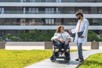 Doctor talking with smiling disabled woman in wheelchair, enjoying sunny day in urban park near