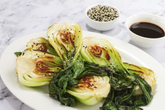 Grilled bok choy served with soy sauce and sesame seeds, on a white plate, homemade, no people
