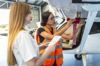 Female aircraft maintenance engineer inspecting airplane wing with pilot holding checklist in